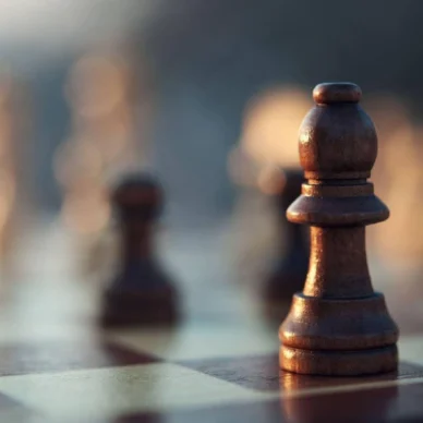 A close-up, low-angle shot of a dark wooden bishop chess piece resting on a chessboard, with other pieces blurred in the background.