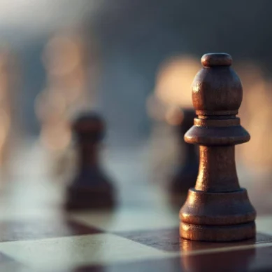 A close-up, low-angle shot of a dark wooden bishop chess piece resting on a chessboard, with other pieces blurred in the background.