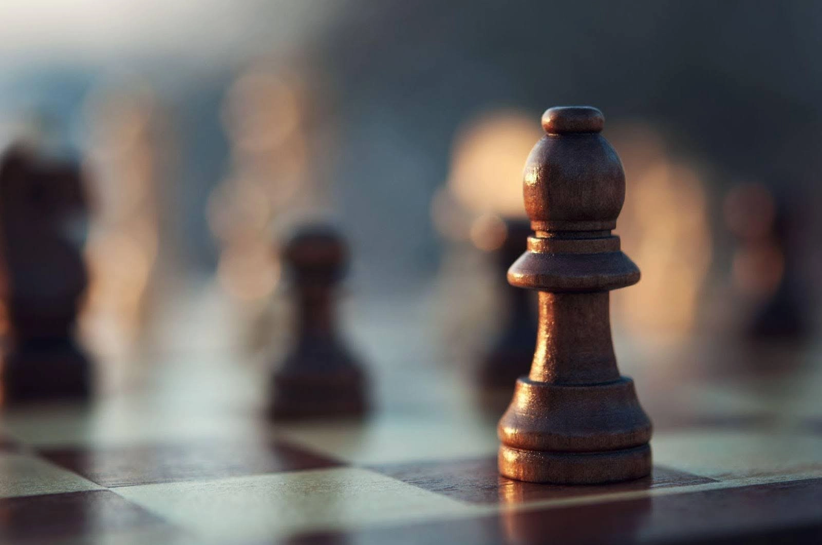 A close-up, low-angle shot of a dark wooden bishop chess piece resting on a chessboard, with other pieces blurred in the background.